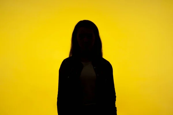 No name, anonymous person hiding face in shadow, human identity. Silhouette portrait of unknown woman standing alone, indoor studio shot, isolated on yellow background