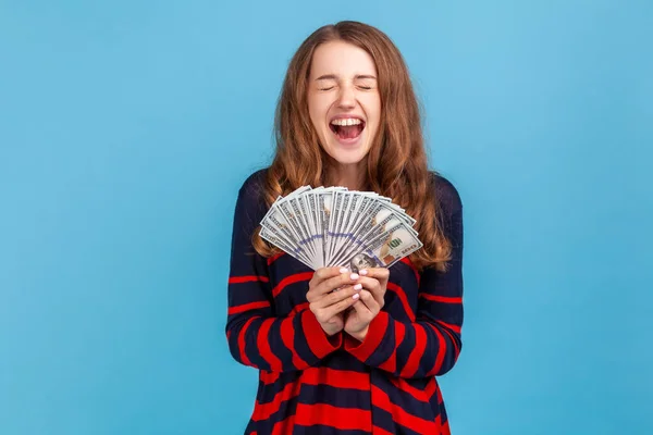 金持ちの興奮した女性は 手の中に多くのドル紙幣を保持縞カジュアルスタイルのセーターを着て 宝くじを獲得し 喜んで叫んで 青い背景に隔離された屋内スタジオショット — ストック写真