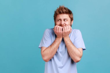 Anxiety disorder. Portrait of stressed out, worried bearded man biting nails, nervous about troubles, panicking and looking scared. Indoor studio shot isolated on blue background.