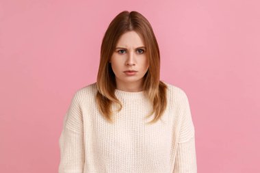 Portrait of young adult angry serious blond woman looking at camera with strict negative expression, aggression, wearing white sweater. Indoor studio shot isolated on pink background.