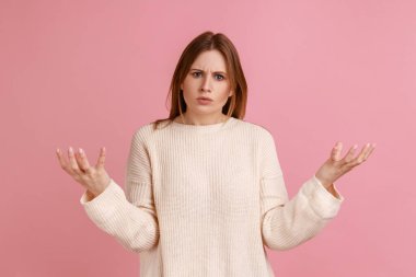Blond woman raise hands to the sides and don't know right answer, negative human emotions, life perception and attitude, wearing white sweater. Indoor studio shot isolated on pink background.