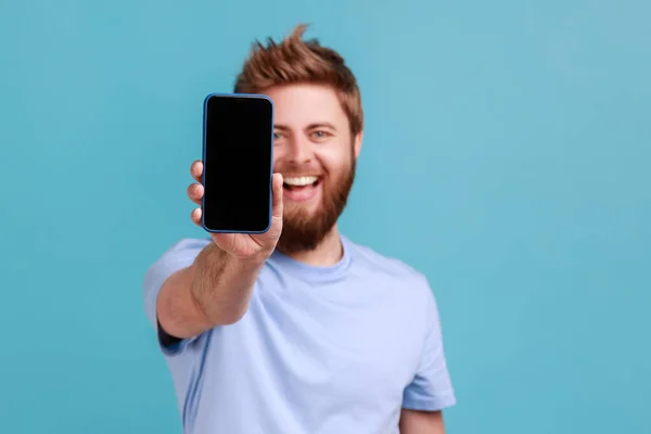 Portrait Bearded Man Holding Out Mobile Phone Looking Camera Toothy — Stockfoto