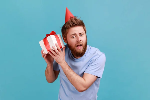 Portrait Surprised Bearded Man Wearing Party Cone Holding White Wrapped – stockfoto