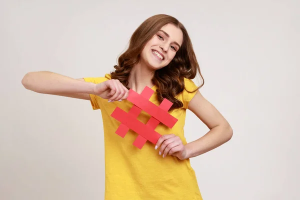 Cheerful Satisfied Teenager Girl Yellow Shirt Showing Holding Red Hashtag — Zdjęcie stockowe