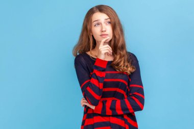 Düşünceli bir kadın, çizgili bir süveter giyiyor şaşkın yüz ifadesiyle kafa patlatıyor, kuşkuları ve tereddütleri olduğuna karar veriyor. Mavi arka planda kapalı stüdyo çekimi.