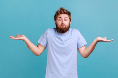 Kimin umurunda? Kafası karışmış sakallı adamın portresi avuçlarını tereddütle yayar hiçbir fikri yoktur ya da kafası karışmıştır, kameraya çaresizce bakar. Mavi arka planda kapalı stüdyo çekimi.