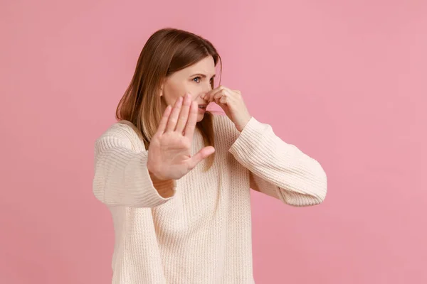 女人捏鼻子 屏住呼吸以避免难闻的气味 并表现出停止的姿态 厌恶恶臭的屁臭味 穿着白色毛衣的形象 在粉色背景下被隔离的室内拍摄 — 图库照片