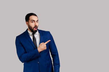 Şaşırmış bir ifadeyle kameraya bakan sakallı adam, fotokopi alanını işaret ediyor, resmi stil kıyafeti giyiyor. Gri arka planda izole edilmiş kapalı stüdyo görüntüleri.