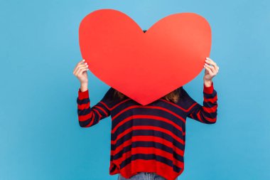 Bilinmeyen bir kadın, çizgili sıradan bir süveter giyiyor, yüzünü büyük kırmızı bir kalple kaplıyor, elinde aşkın sembolü, isimsiz bir hayır kurumu ve bakım var. Mavi arka planda kapalı stüdyo çekimi.