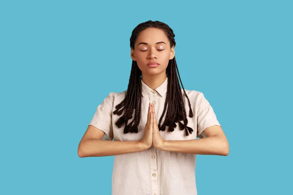 迷人迷人的黑发女子手握瑜伽姿势 面部表情平静 手心紧握 闭着眼睛 室内拍摄被蓝色背景隔离 — 图库照片