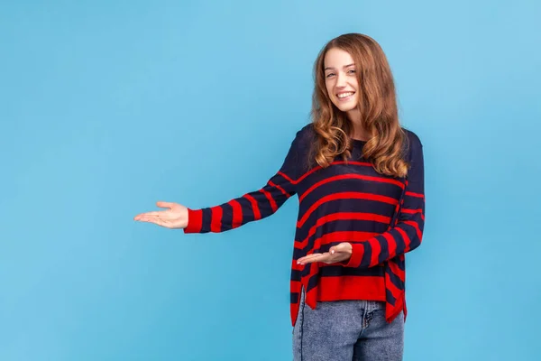 縞模様のカジュアルなスタイルのセーターを着て笑顔の女性の肖像画は 広い腕を上げて立って歓迎またはカメラを見て 笑顔を共有する 青い背景に隔離された屋内スタジオショット — ストック写真