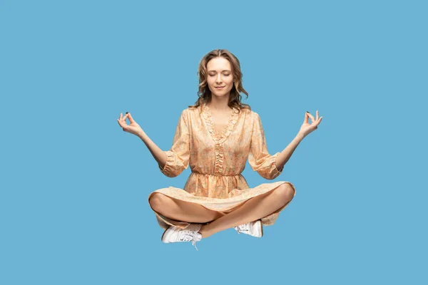 Hovering in air. Calm peaceful relaxed girl ruffle dress levitating with mudra gesture hands up, closed eyes, meditating sitting in yoga position. indoor studio shot isolated on gray background