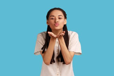 Romantik güzel bir kadın hava öpücüğü veriyor, dudaklarını ağıza doğru kıvırıyor, mwah coquettish gönderiyor, ortağını neşelendirmek istiyor. Mavi arka planda kapalı stüdyo çekimi.