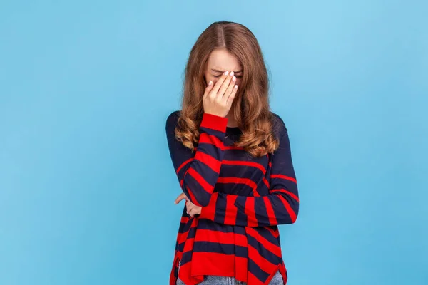 縞模様のカジュアルなスタイルのセーターを着て動揺した若い女性が彼女の頭をお辞儀をし 絶望的な悲しい気持ちを経験する 青い背景に隔離された屋内スタジオショット — ストック写真