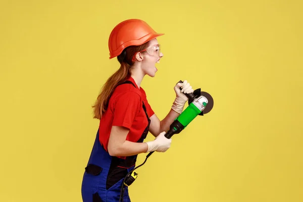 분쇄기를 가지고 일하는 작업복을 보호용 헬멧을 스튜디오 가노란 배경에 고립된 — 스톡 사진