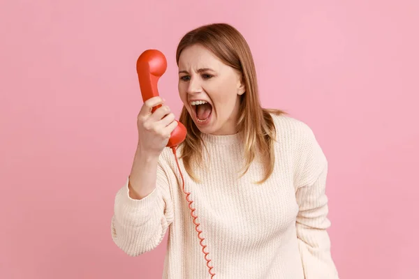 怒った金髪の女性が赤い携帯電話に叫んで 不快な会話をし 侵略を表現し 白いセーターを着ていた肖像画 ピンクの背景に隔離された屋内スタジオショット — ストック写真