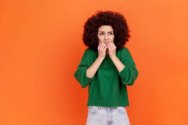 緑のカジュアルなスタイルのセーター立って指の爪をかむ 心配を着てアフロの髪型と神経ストレスの女性の肖像画 オレンジの背景に隔離された屋内スタジオショット — ストック写真