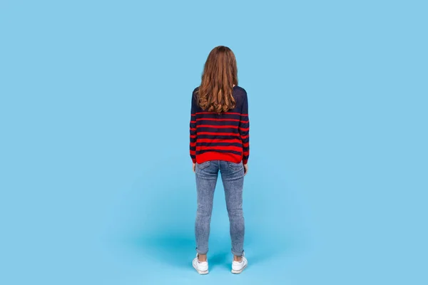女性の縞模様のカジュアルなスタイルのセーターを着ての完全な長さの背中の肖像画 距離を見て落ち着いて立って 待って 後方にポーズ 青い背景に隔離された屋内スタジオショット — ストック写真