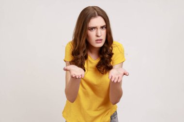 Nasıl yapabildin? Sarı tişörtlü, hayal kırıklığına uğramış genç bir kızın portresi. Ellerini kaldırıp ne istediğini soruyor. Kızgın surat. Gri arka planda izole edilmiş kapalı stüdyo görüntüleri.