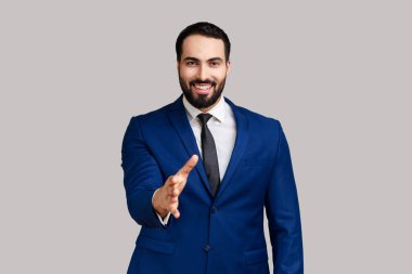 Pozitif sakallı adam el sıkışıyor ve gülümsüyor dost canlısı, danışman ya da İK yöneticisi iş teklif ediyor, ortaklık, resmi stil kıyafeti giyiyor. Gri arka planda izole edilmiş kapalı stüdyo görüntüleri.