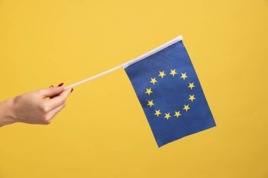 Profil tarafı, Eroupean sendikası bayrağını tutan kadının yakın çekimi. Sarı arka planda kapalı stüdyo çekimleri.