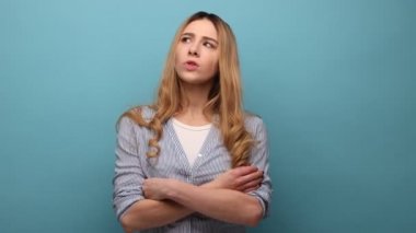 Dalgalı saçlı, düşünceli, çene tutan, başka tarafa bakan, derin düşünceler içinde, çizgili gömlek giyen genç bir kadının portresi. Mavi arka planda kapalı stüdyo çekimi.