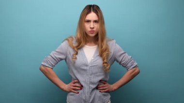 Genç, sinirli, ciddi, sarışın bir kadının resmi. Kameraya kötü bir ifadeyle bakıyor. Saldırganlık, kalça elele tutuşmak, çizgili gömlek giymek. Mavi arka planda kapalı stüdyo çekimi.