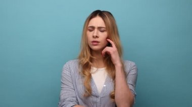 Ciddi sorunlarla uğraşan, tereddütlü bir ifadeyle bakan, zor seçimler yapan, çizgili gömlek giyen düşünceli üzgün bir kadının portresi. Mavi arka planda kapalı stüdyo çekimi.