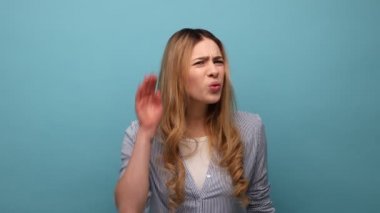 Kafası karışmış bir kadının portresi, daha iyi dinlemek için elini kulağına yaklaştırıyor, işitme sorunları yaşıyor, anlaması zor, çizgili gömlek giyiyor. Mavi arka planda kapalı stüdyo çekimi.