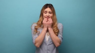 Dalgalı saçlı, gergin genç bir kadının portresi. Sakinleşmeye çalışıyor ve yoga pratiğiyle rahatlamaya çalışıyor. Çizgili gömlek giyiyor. Mavi arka planda kapalı stüdyo çekimi.