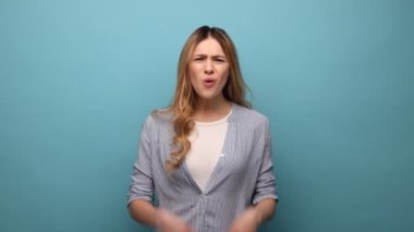 Bunu nasıl yaparsın? Kızgın bir kadının portresi, kollarını kaldırması, başarısızlığın nedenini sorması, kavga etmesi, çizgili gömlek giymesi. Mavi arka planda kapalı stüdyo çekimi.