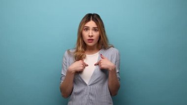 Kendini gösteren, kameraya bakan, korku hisseden, hayır başını sallayan, çizgili gömlek giyen mutsuz genç bir kadının portresi. Mavi arka planda kapalı stüdyo çekimi.