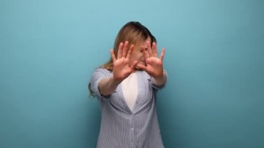 Buna daha fazla bakmak istemiyorum. Utangaç, kafası karışık bir kadının portresi. Gözleri eliyle kapatıyor. Utanmış ve izlemeye korkuyor. Mavi arka planda kapalı stüdyo çekimi.