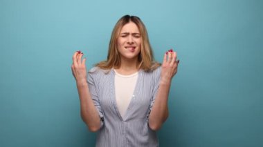 Umut dolu, dalgalı saçlı, parmakları çapraz duran çekici bir kadının portresi çizgili gömlek giyerek hayallerinin gerçekleşmesini diliyor. Mavi arka planda kapalı stüdyo çekimi.