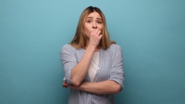 Genç ve çekici bir kadının portresi. Dalgalı saçları olan, ağzını kapatan, kimseye söylemeyen, çizgili gömlek giyen. Mavi arka planda kapalı stüdyo çekimi.