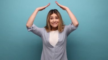 Dalgalı saçlı, ev yapımı jest ve gülümseme yapan çekici bir kadının portresi. Hayat sigortası, koruma, çizgili gömlek. Mavi arka planda kapalı stüdyo çekimi.