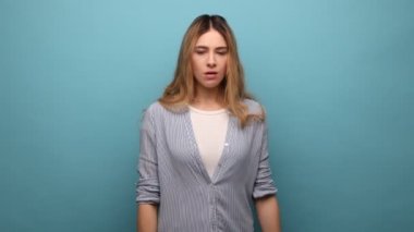 Kırgın, dalgalı saçlı, çıkış yapan, onu yalnız bırakmayı talep eden, sinirli bir ifadeyle geri dönen, çizgili gömlek giyen bir kadın. Mavi arka planda kapalı stüdyo çekimi.