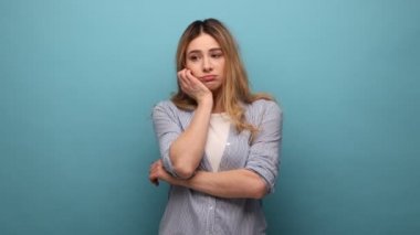 Sıkıcı tembel kadın eline yaslanıp kameraya ilgisiz bir şekilde bakıyor, sıkıcı bir hikaye dinliyor, sonuçtan hayal kırıklığına uğruyor, çizgili gömlek giyiyor. Mavi arka planda kapalı stüdyo çekimi.