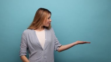 Ticari teklife bak. Avucundaki fotokopi alanını gösteren bir kadın. Fikir sunumu için boş bir yer. Ürün reklamcılığı. Mavi arka planda kapalı stüdyo çekimi.