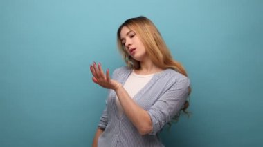 Tırnaklarına bakan güzel bir kadının portresi, taze manikürle hayran olmak, güzellik prosedürlerinden zevk almak, kendine dikkat etmek, çizgili gömlek giymek. Mavi arka planda kapalı stüdyo çekimi.