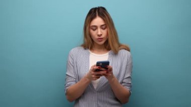 Akıllı telefon kullanan, mesaj yazan ya da sosyal ağları kontrol eden, yazı yazan, ciddi ifade veren, çizgili gömlek giyen odaklı kadın portresi. Mavi arka planda kapalı stüdyo çekimi.