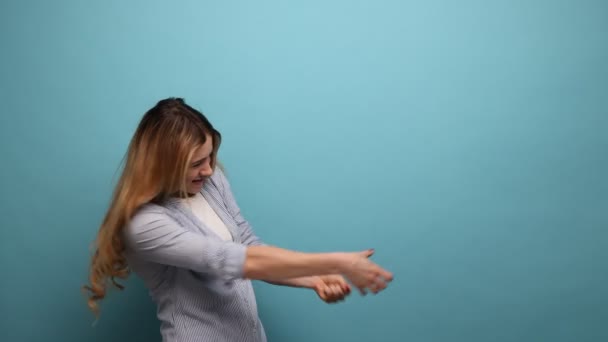 飼育された拳で立って積極的な目的の若い女性のサイドビューの肖像画は ストライプのシャツを着て スミスをプルする努力をする 青い背景に隔離された屋内スタジオショット — ストック動画