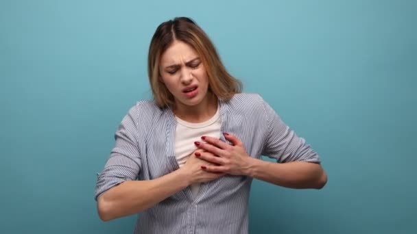 脳卒中のリスク 心臓発作 縞模様のシャツを着て胸に手をつないで不健康な女性の肖像画 青い背景に隔離された屋内スタジオショット — ストック動画