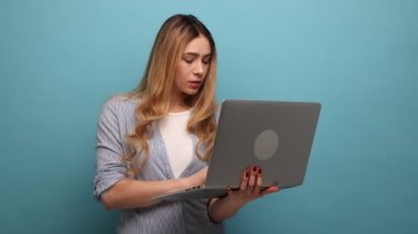 Dizüstü bilgisayarda çalışan ciddi dalgalı saçlı çekici bir kadının portresi. Dikkatlice ekrana bakıyor, çizgili gömlek giyiyor. Mavi arka planda kapalı stüdyo çekimi.