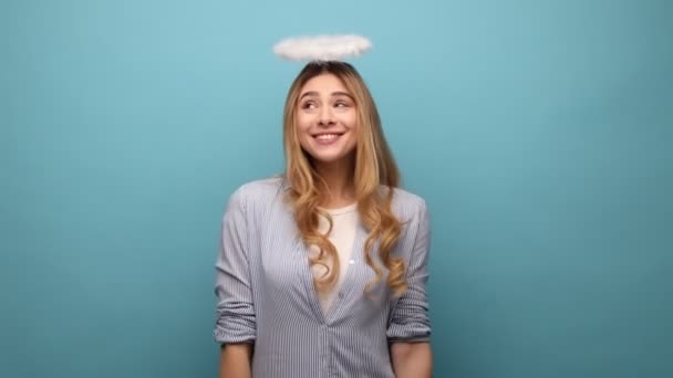 迷人的年轻天使般的成年女子 头戴灵巧的头巾 表达积极的情感 庆祝节日 穿着条纹衬衫 室内拍摄被蓝色背景隔离 — 图库视频影像