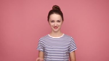 Kurnaz, kurnaz, güzel bir kadın kameraya bakıyor, kurnaz bir şeyler planlıyor, birine şaka yapıyor, çizgili tişört giyiyor. Pembe arka planda kapalı stüdyo çekimleri.