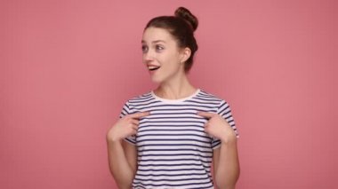 Vay canına, bu ben miyim? Saçları topuzlu, ağzı açık kameraya bakan, kendini şoka sokan, çizgili tişört giyen şaşırmış bir kadın. Pembe arka planda kapalı stüdyo çekimleri.