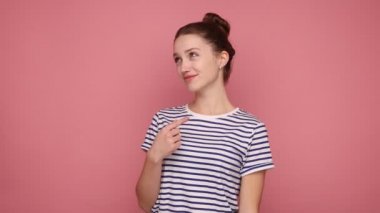 Ben buyum. Kıllı topuzu olan kibirli, kendini beğenmiş, gururlu ve kendini beğenmiş, egosu büyük, çizgili tişört giyen bir kadın. Pembe arka planda kapalı stüdyo çekimleri.