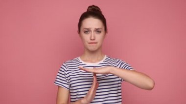 Daha fazla zamana ihtiyacım var, yeterli sınıra. Hoşnutsuz bir kadın el hareketi yapıyor, yalvararak bakıyor, son teslim tarihinden endişe ediyor, çizgili tişört giyiyor. Pembe arka planda kapalı stüdyo çekimleri.