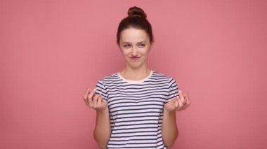 Çekici bir kadın ayakta durup kameraya parayla bakıyor ya da elinde İtalyan jesti, banknotlar savurduğunu, çizgili tişört giydiğini hayal ediyor. Pembe arka planda kapalı stüdyo çekimleri.